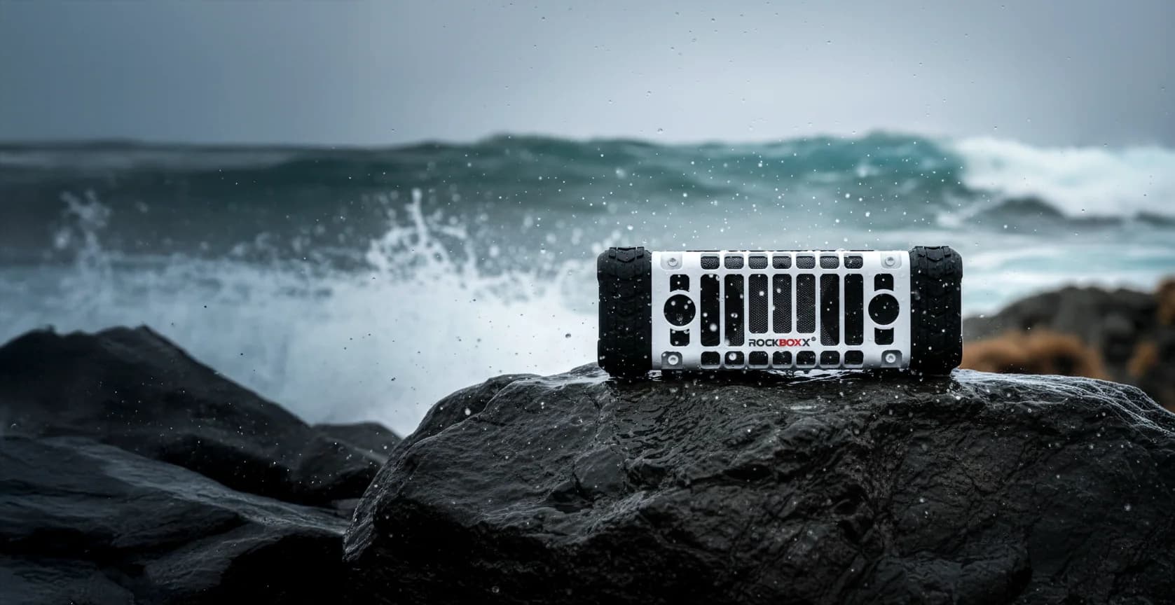 Rugged Bluetooth speaker on a wet rock as ocean waves crash behind it